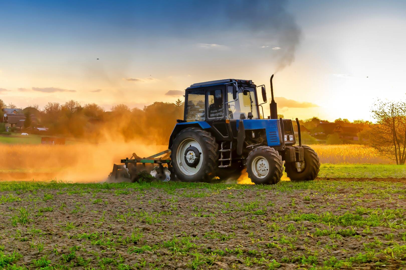 Modern blue tractor machinery plowing agricultural field meadow at farm at spring autumn during sunset.Farmer cultivating,make soil tillage before seeding plants,crops,nature countryside rural scene.